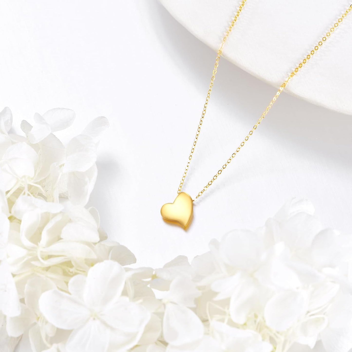 Asymmetric 14K yellow gold heart pendant necklace styled with white flowers.